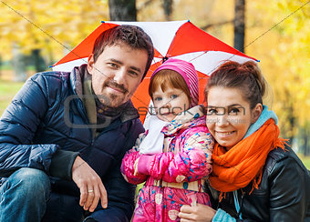 Happy young family under an umbrella in an autumn park