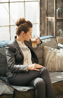 Business woman sitting on sofa and drinking coffee in loft