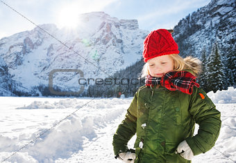 Child in green coat standing in the front of snowy mountains