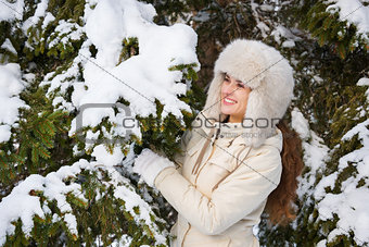 Happy young woman standing outdoors near snowy spruce branch