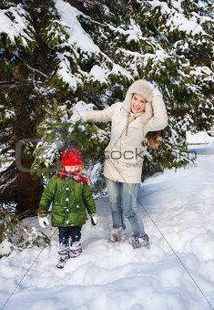 Mother shaking snow off branch on child while standing outdoors