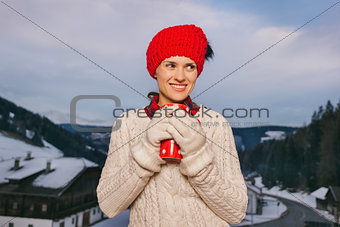 Woman with red cup on balcony overlooking mountains in evening