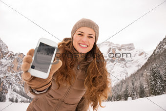 Woman outdoors among snow-capped mountains showing cell phone