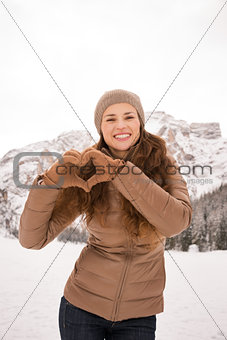 Woman showing heart shaped hands among snow-capped mountains