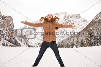 Happy young woman jumping outdoors among snow-capped mountains