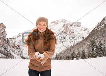 Smiling woman with snowball outdoors among snow-capped mountains