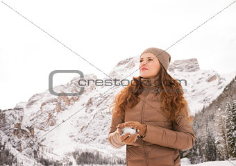 Young woman making snowball outdoors among snow-capped mountains