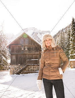 Happy young woman standing in the front of cosy mountain house