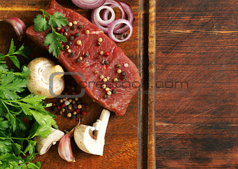 Fresh raw beef meat on a cutting board with vegetables and spices
