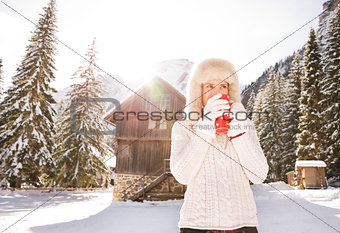 Woman in white sweater enjoying hot beverage near mountain house