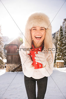 Smiling woman with red cup standing near cosy mountain house