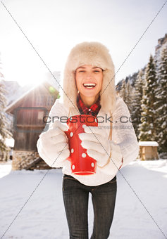 Closeup on red cup in hands of smiling woman near mountain house