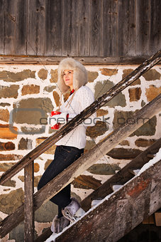 Young woman with cup standing on stairs of cosy mountain house