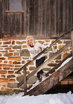 Happy woman in white sweater on stairs of cosy mountain house