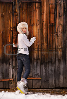 Woman in white sweater and furry hat posing near wood wall