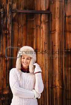 Woman in white knitted sweater standing near rustic wood wall