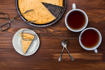 New York cheesecake on rustic wooden background with cup of tea, tongs for dessert and yellow daffodil.