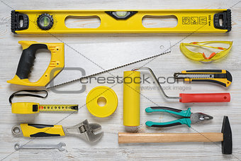 Top view of construction instruments and tools on wooden DIY workbench. Level, saw, glasses, tape measure, wrench, spanner,paint roll, hammer, cutter, pliers.