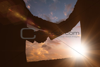 Composite image of silhouettes shaking hands