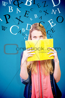 Composite image of student covering face with book in library