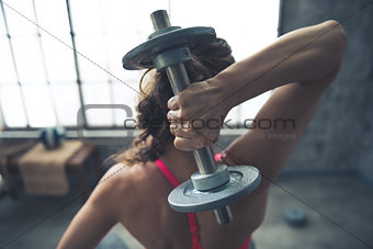 Seen from behind fitness woman lifting dumbbell