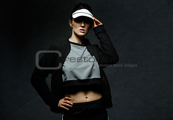Young fit woman adjusting tennis visor against dark background