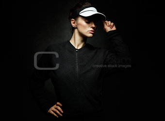 Woman athlete adjusting tennis visor against dark background