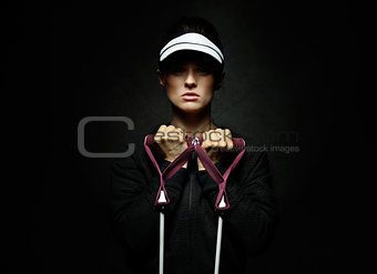 Young fit woman holding resistance band against black background
