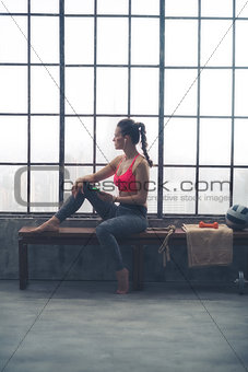 Fitness woman with cell phone sitting in loft gym