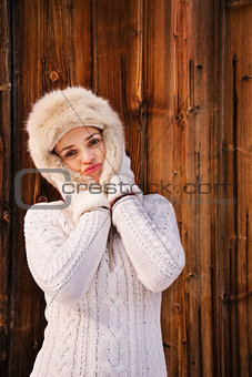 Happy woman fooling around with furry hat near rustic wood wall