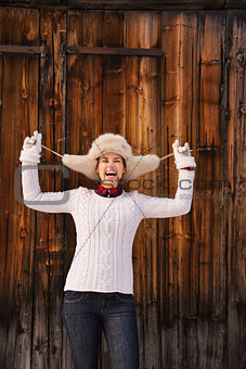Smiling woman fooling around with furry hat near wood wall
