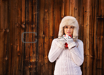 Woman in white knitted sweater with cup near rustic wood wall