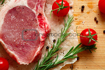 Pieces of crude meat with rosemary and tomatoes.
