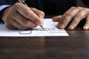 Man signing a document or writing correspondence with a close up view of his hand with the pen and sheet of notepaper on a desk top. With retro filter effect.