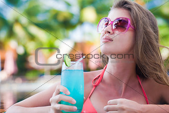 Beautiful woman with tropical cocktail in the pool