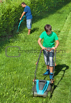 Boy mowing the lawn with man trimming at the edges