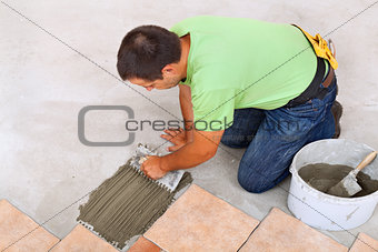 Man laying ceramic tiles floor - spreading the adhesive