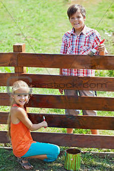 Young boy and girl painting a wooden fence