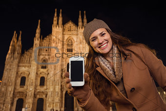 Smiling woman showing cell phone near Duomo in evening, Milan