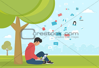 Young man sitting in the park under a tree and working with laptop