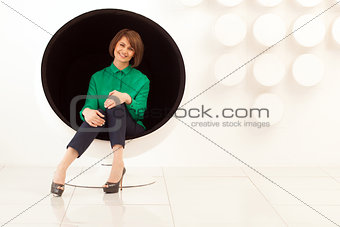 Attractive woman sitting on spherical chair with hands on knees