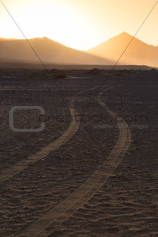 Wheel tracks in sand and dramatic landscape.