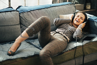Happy young woman laying on the couch and listening to the music