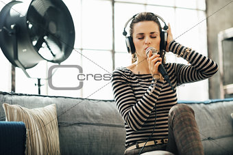 Woman in headphones singing into a microphone in loft apartment