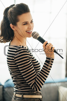 Happy young woman singing into a microphone in loft apartment