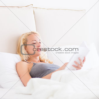 Young Caucasian woman reading in bed.