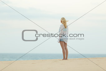 Woman on sandy beach in white shirt at dusk.
