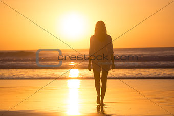 Lady walking on sandy beach in sunset.