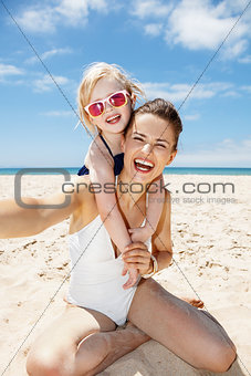 Smiling mother and daughter in swimsuits taking selfies at beach