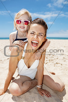 Smiling mother and daughter in swimsuits at sandy beach
